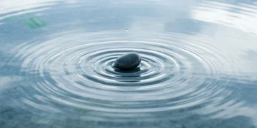 A smooth river stone creating expanding ripples in a still pool of water, symbolizing the widespread effects of social impact and sustainable community growth.